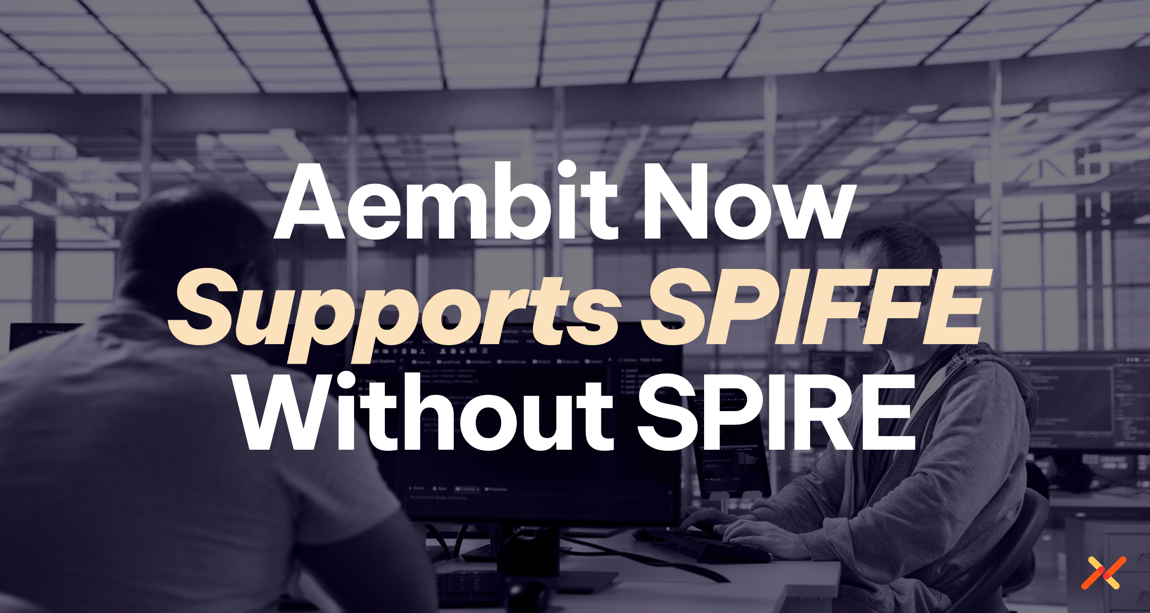 Two developers at computer workstations with text reading “Aembit Now Supports SPIFFE Without SPIRE.”